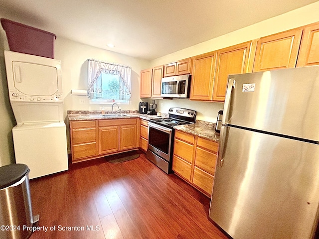 kitchen with sink, stacked washing maching and dryer, dark hardwood / wood-style flooring, light stone counters, and stainless steel appliances