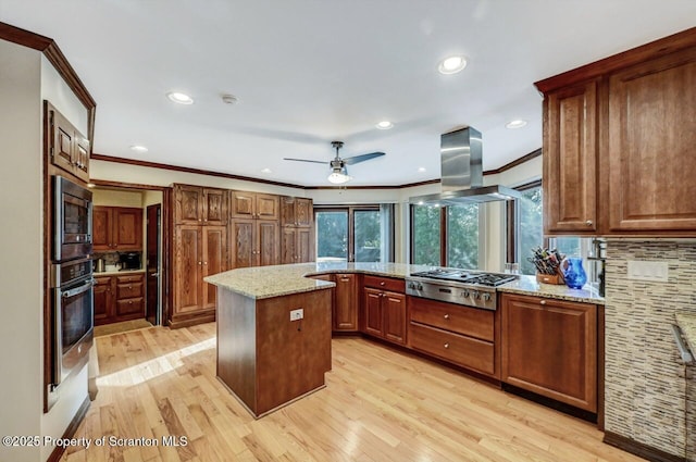 kitchen with island exhaust hood, appliances with stainless steel finishes, a center island, and light stone counters