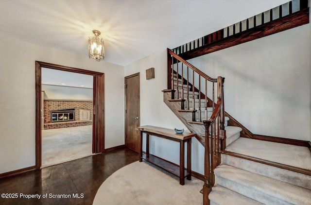 staircase featuring a brick fireplace and a chandelier