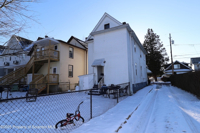 snow covered rear of property featuring a balcony, entry steps, and fence