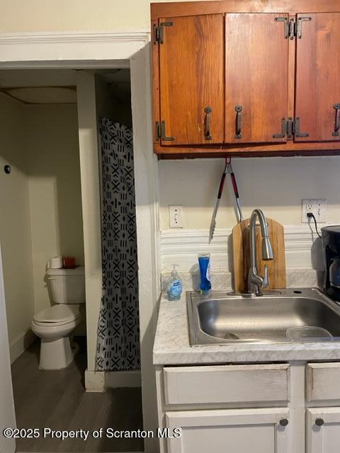 kitchen with brown cabinets, light countertops, wood finished floors, a sink, and baseboards