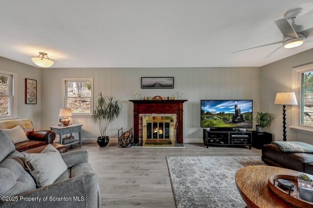 living area featuring light wood finished floors, a fireplace, a ceiling fan, and baseboards