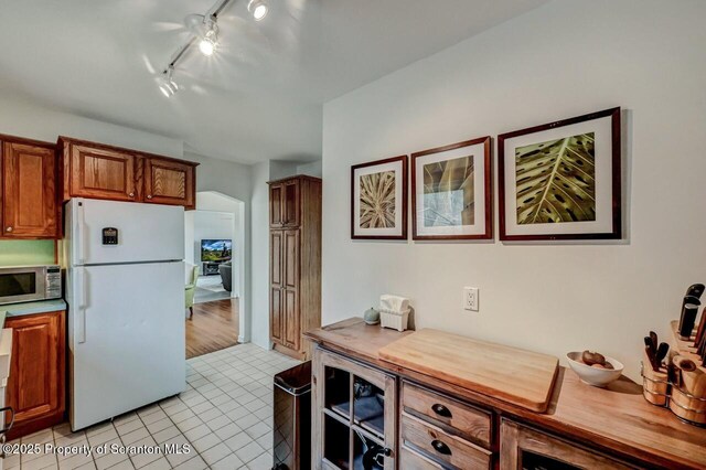 kitchen with brown cabinets, light countertops, stainless steel microwave, freestanding refrigerator, and light tile patterned flooring