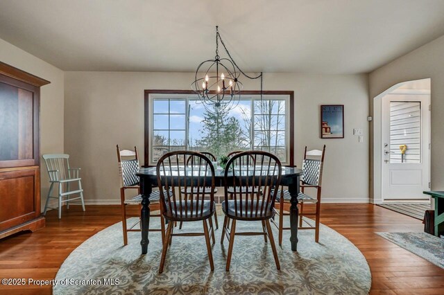 dining area with an inviting chandelier, baseboards, arched walkways, and dark wood-type flooring