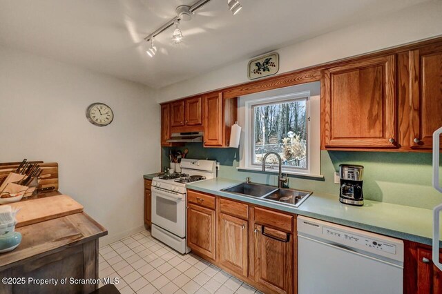 kitchen with white appliances, brown cabinetry, light countertops, under cabinet range hood, and a sink