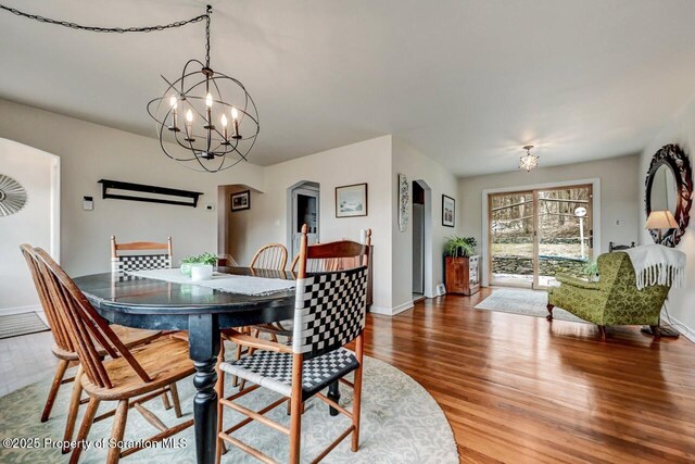 dining room with arched walkways, a notable chandelier, baseboards, and wood finished floors