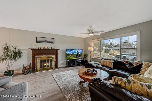 living room featuring a ceiling fan, a glass covered fireplace, baseboards, and light wood finished floors