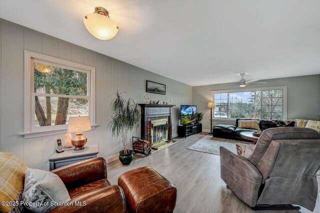 living area with light wood-type flooring, a fireplace with flush hearth, baseboards, and a ceiling fan