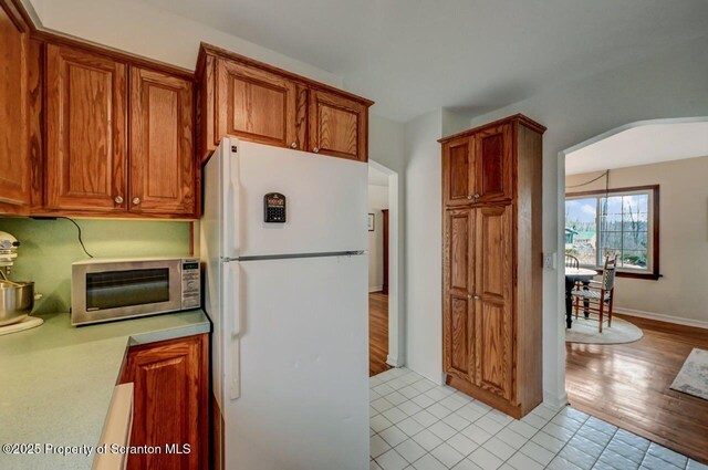 kitchen with brown cabinetry, freestanding refrigerator, light countertops, and arched walkways