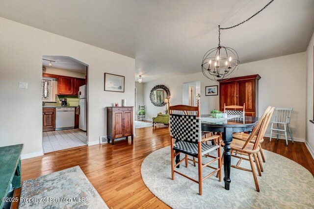 dining area featuring arched walkways, visible vents, an inviting chandelier, light wood-style floors, and baseboards