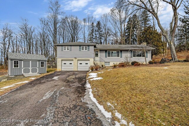 tri-level home featuring aphalt driveway, an attached garage, an outdoor structure, a storage unit, and a front yard