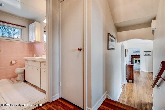 hallway featuring arched walkways, dark wood-style flooring, visible vents, and tile walls