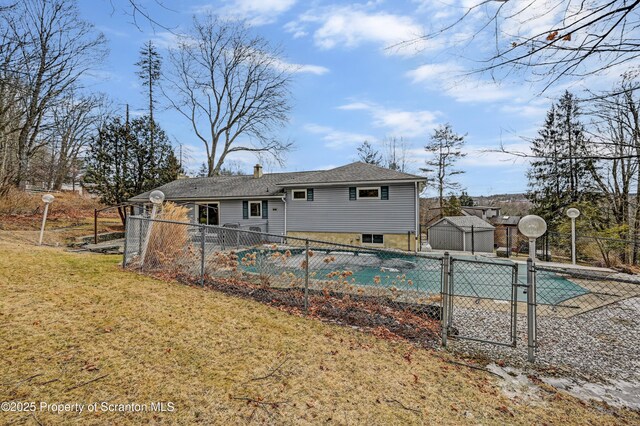 back of property featuring a yard, a covered pool, fence, and an outdoor structure