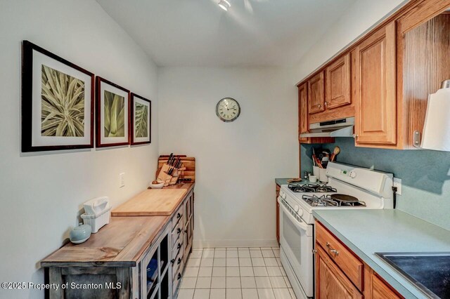 kitchen with light tile patterned floors, light countertops, under cabinet range hood, and white gas range