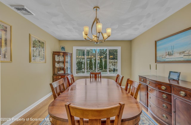 dining space featuring visible vents, light wood-style flooring, baseboards, and an inviting chandelier