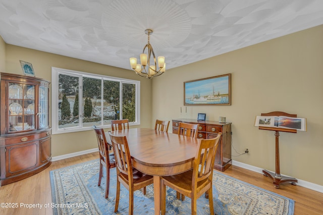 dining space featuring light wood-style floors, baseboards, and a notable chandelier