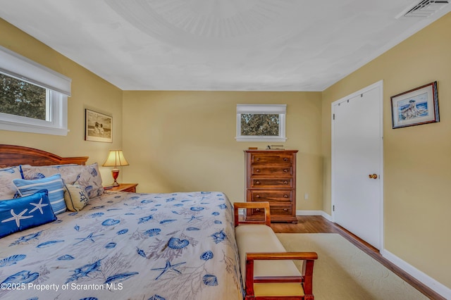 bedroom featuring wood finished floors, visible vents, baseboards, and multiple windows