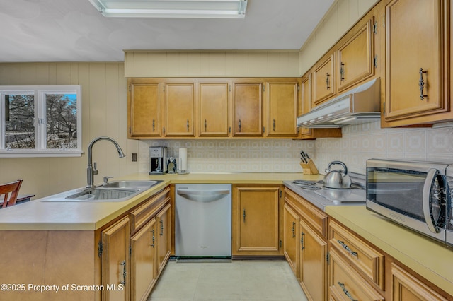 kitchen with under cabinet range hood, stainless steel appliances, a peninsula, a sink, and light countertops