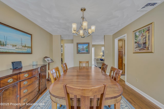 dining area with light wood-style floors, a chandelier, visible vents, and baseboards