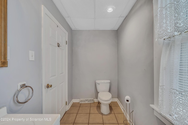 bathroom with toilet, a paneled ceiling, and tile patterned floors