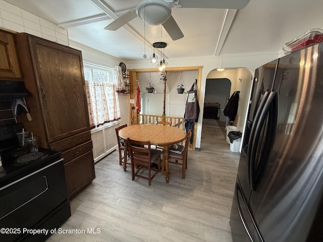 dining area featuring arched walkways, ceiling fan, radiator heating unit, and light wood-style flooring