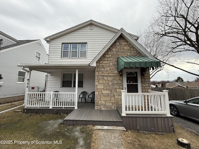 view of front of home with covered porch, stone siding, and fence