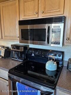 kitchen with black electric range, stainless steel microwave, and dark countertops