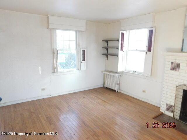 unfurnished living room with radiator, a fireplace, hardwood / wood-style floors, and plenty of natural light