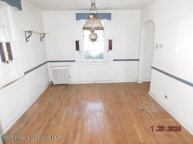 unfurnished dining area featuring wood-type flooring and radiator heating unit