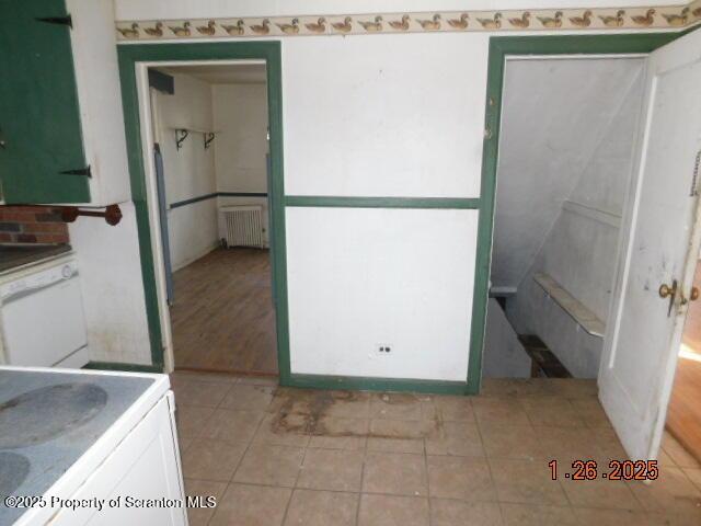 interior space with white dishwasher, radiator, light tile patterned floors, and white cabinets