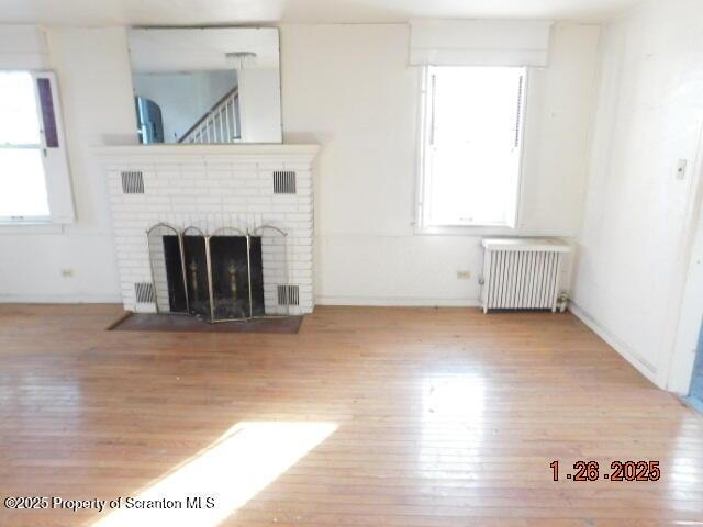 unfurnished living room featuring a brick fireplace, plenty of natural light, radiator heating unit, and light hardwood / wood-style flooring