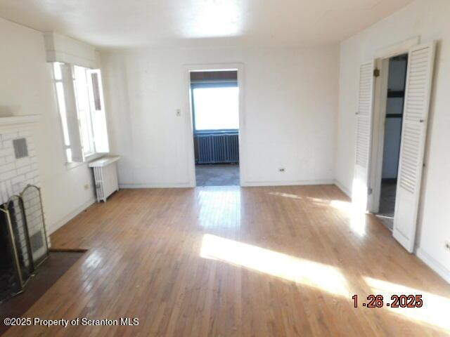 unfurnished living room with radiator, wood-type flooring, and a brick fireplace