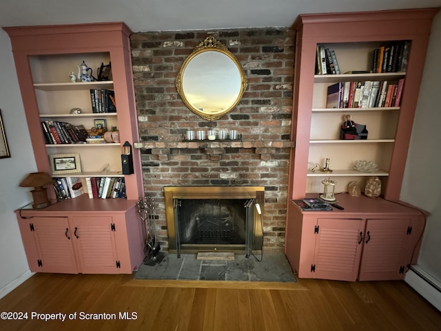 living room with a fireplace, a baseboard radiator, built in features, and hardwood / wood-style flooring