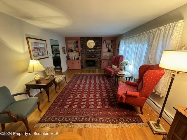 sitting room featuring built in features, a fireplace, a baseboard radiator, and light hardwood / wood-style flooring