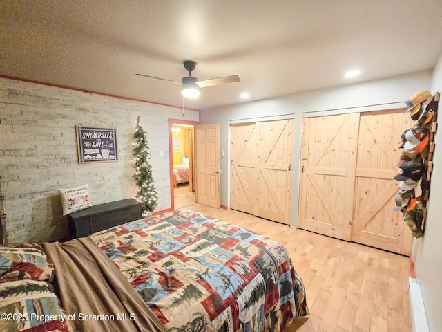 bedroom featuring ceiling fan, brick wall, a barn door, multiple closets, and light wood-type flooring