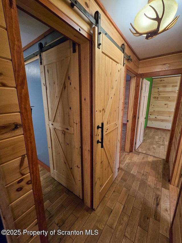 corridor with hardwood / wood-style flooring, a barn door, and wood walls