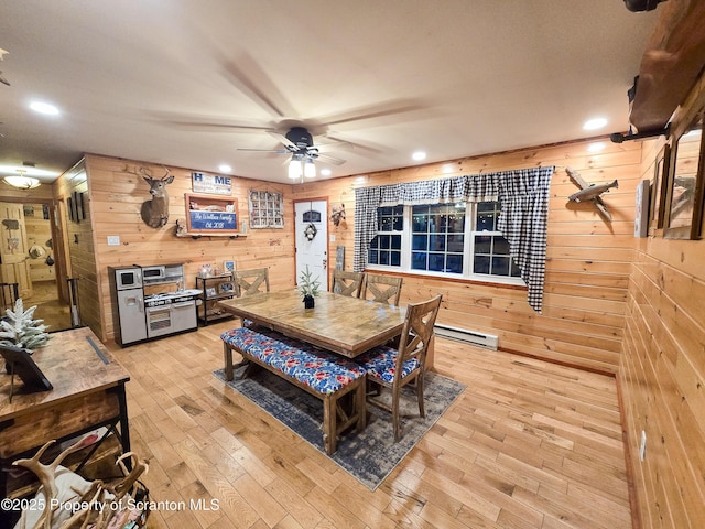 dining area featuring light wood-type flooring, baseboard heating, ceiling fan, and wood walls