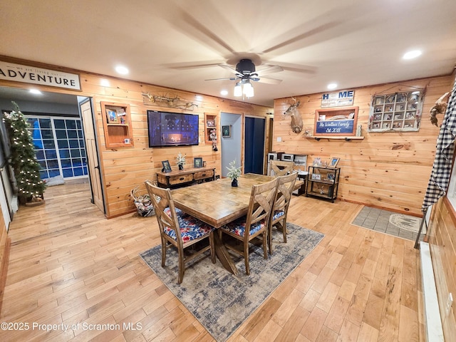 dining space with light wood-type flooring, ceiling fan, and wooden walls