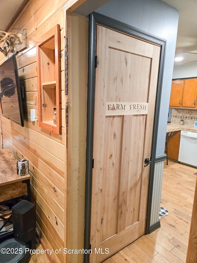 room details featuring hardwood / wood-style flooring, dishwasher, tasteful backsplash, and wood walls