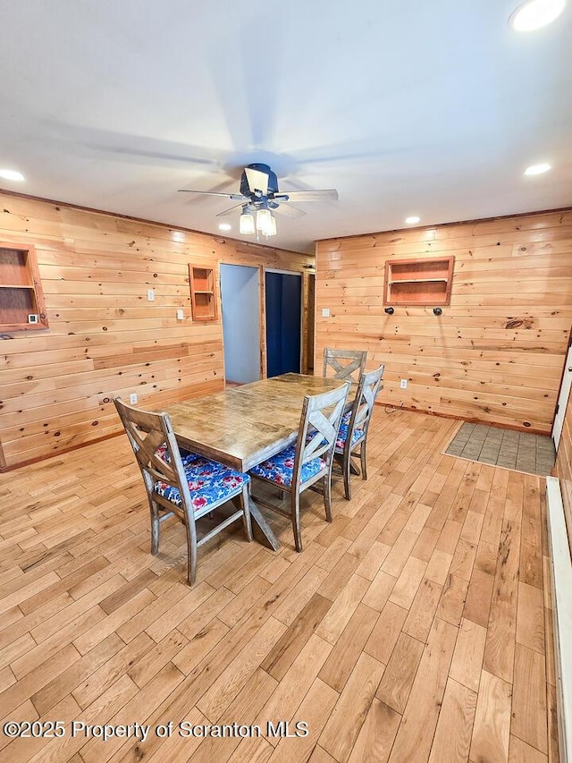 dining space with ceiling fan, wooden walls, and light hardwood / wood-style floors