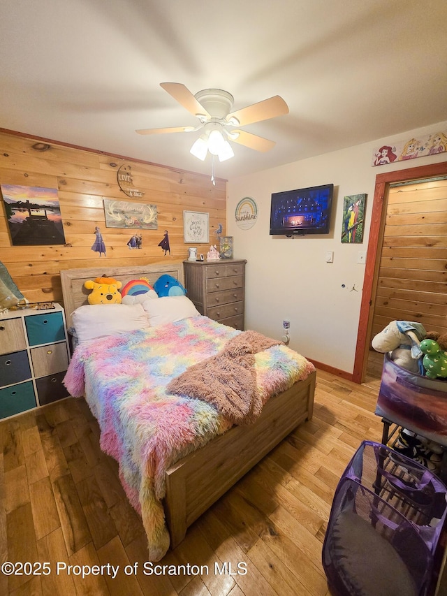 bedroom featuring wooden walls, light hardwood / wood-style floors, and ceiling fan