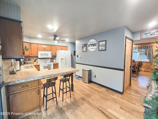 kitchen with a kitchen bar, white appliances, ceiling fan, kitchen peninsula, and light wood-type flooring