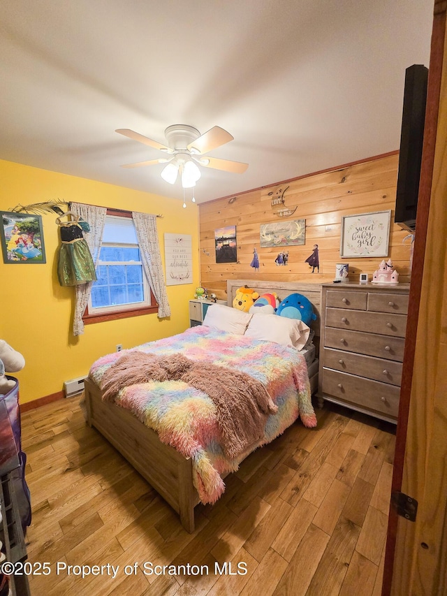 bedroom featuring a baseboard heating unit, wood walls, ceiling fan, and light hardwood / wood-style flooring