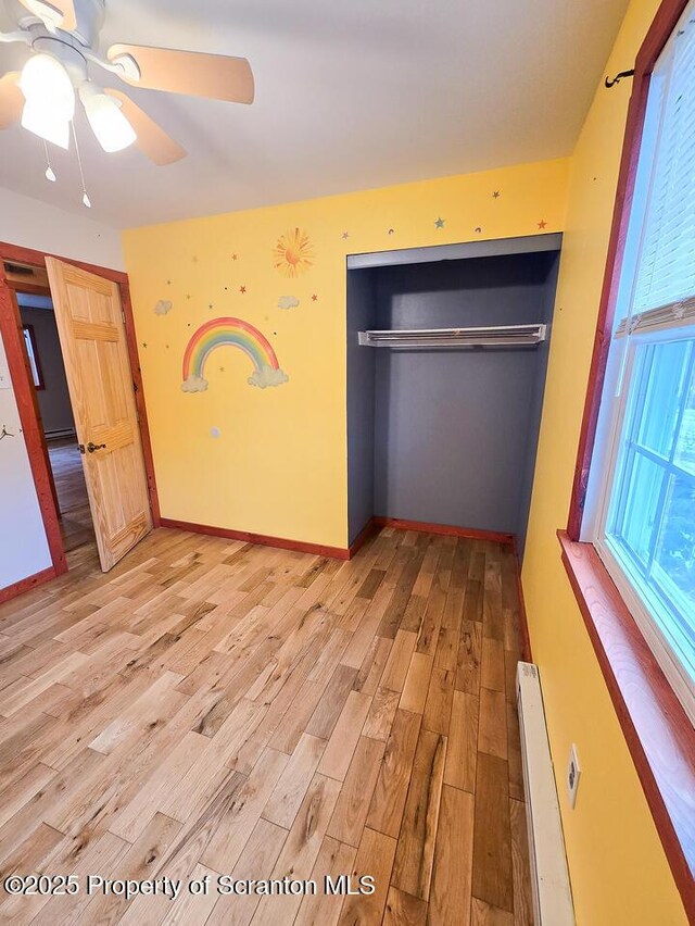 unfurnished bedroom featuring baseboard heating, ceiling fan, light hardwood / wood-style floors, and a closet