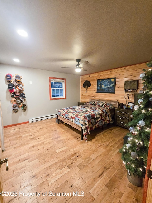 bedroom with ceiling fan, wooden walls, light hardwood / wood-style flooring, and a baseboard heating unit