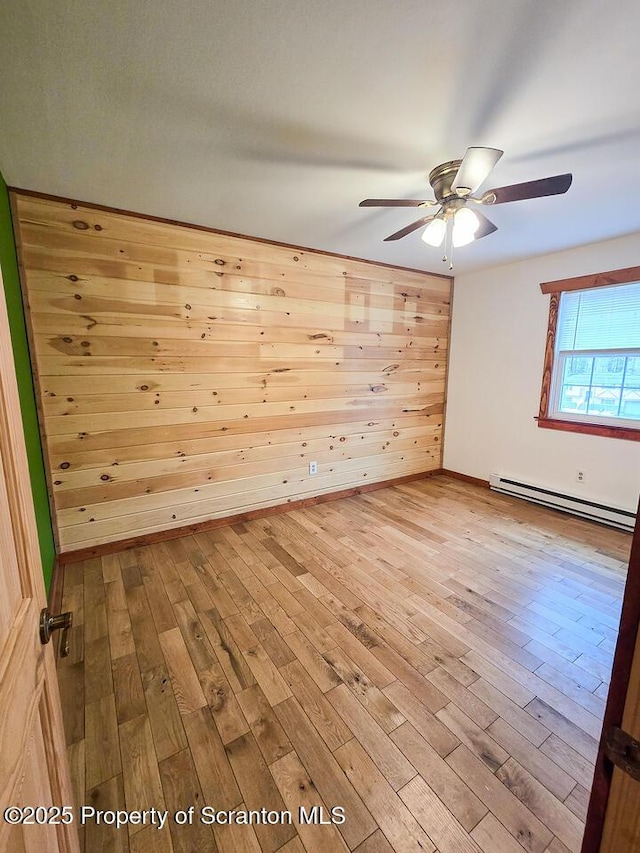 spare room featuring ceiling fan, wooden walls, light hardwood / wood-style floors, and a baseboard heating unit