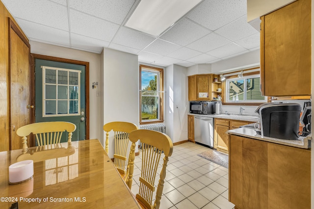 kitchen with a drop ceiling, sink, stainless steel dishwasher, light tile patterned floors, and radiator heating unit