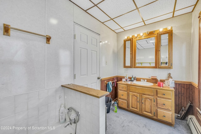 bathroom with a paneled ceiling, vanity, wood walls, a tub to relax in, and a baseboard radiator