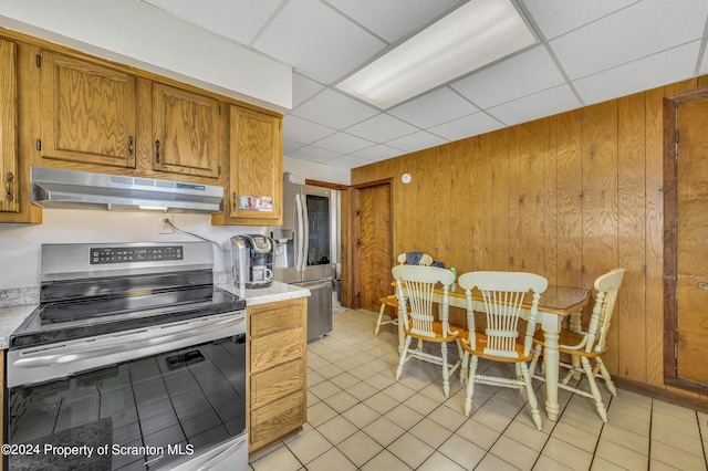 kitchen featuring a drop ceiling, wood walls, light tile patterned floors, and appliances with stainless steel finishes