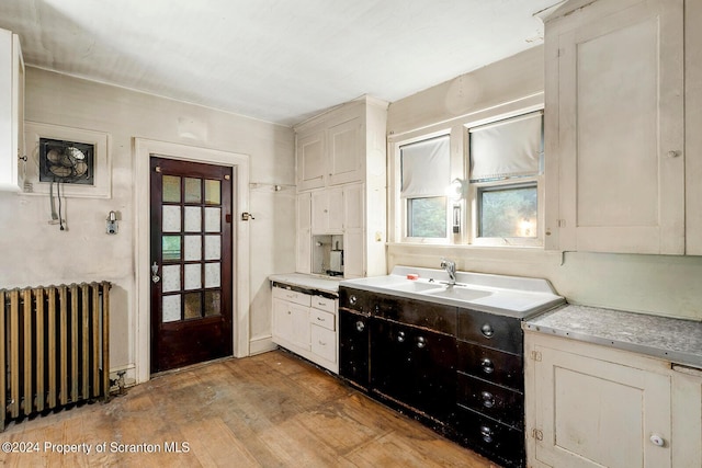 kitchen with radiator, sink, white cabinets, and light wood-type flooring